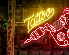 Letrero neón con diseño de máquina de tatuajes y palabra Tattoo en vidriera