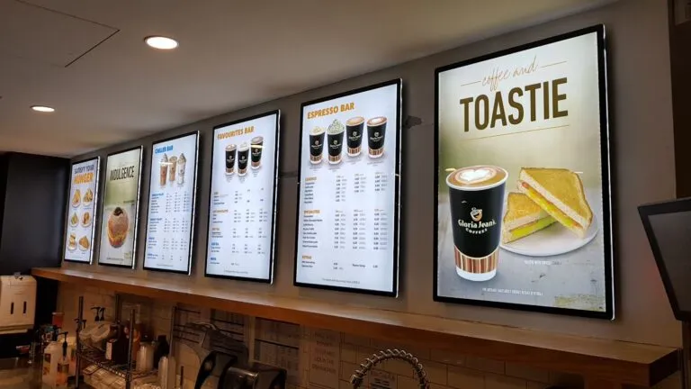 Pantallas digitales con menú de bebidas, espresso y sándwiches en cafetería Gloria Jean’s